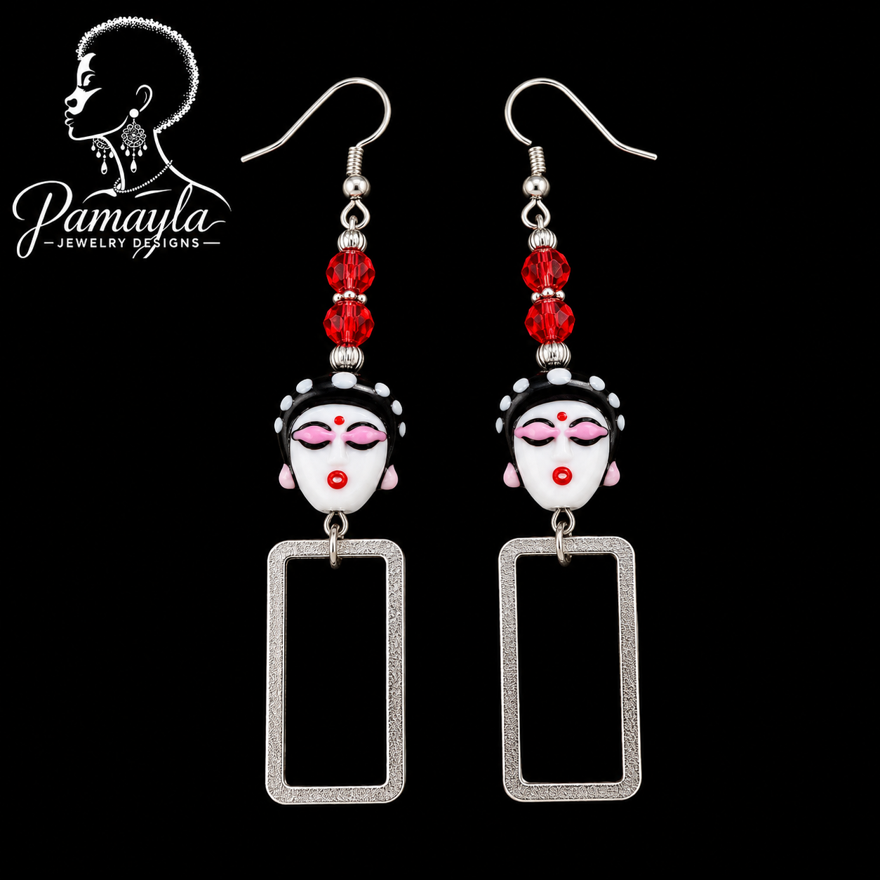Pair of earrings with face designs and red beads on a black background, featuring the brand 'Pamayla Jewelry Designs'.